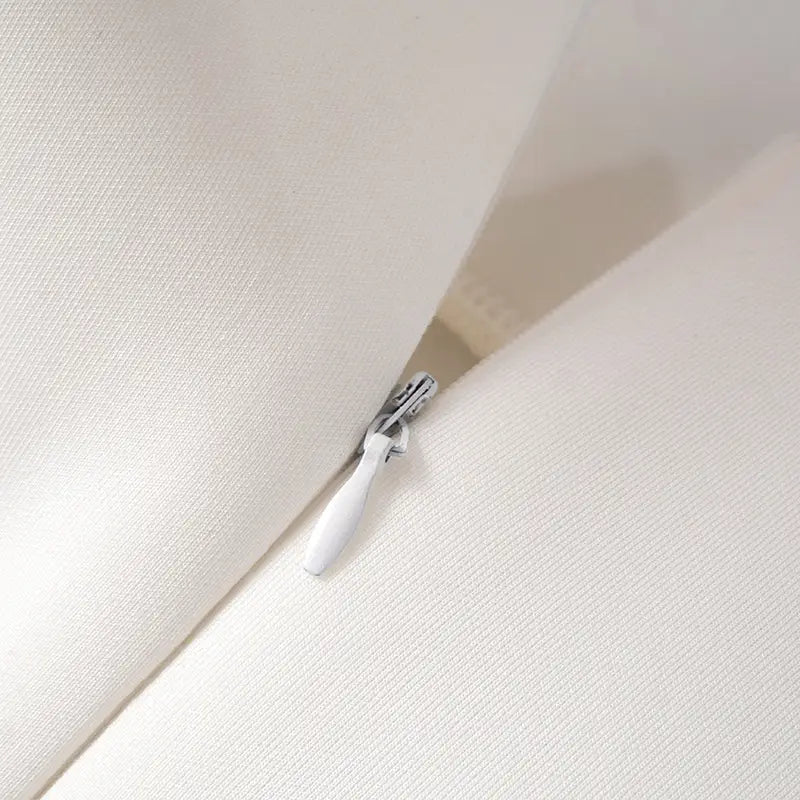 White zipper pull with a sleek metallic slider on the back of a women’s strapless a line mini dress with fitted bodice made from soft textured cream-colored fabric.