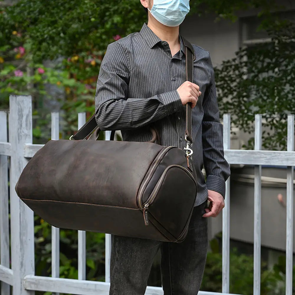Dark brown leather duffle bag with zipper closure and adjustable shoulder strap designed as a vintage large folding travel bag.