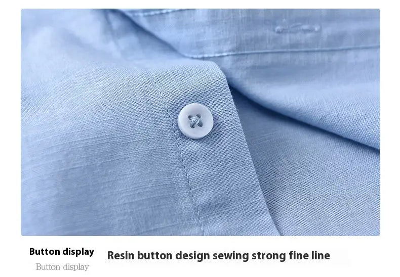 A white resin button with a subtle cross design sewn onto light blue linen fabric of a Chinese style linen mandarin collar shirt for men.