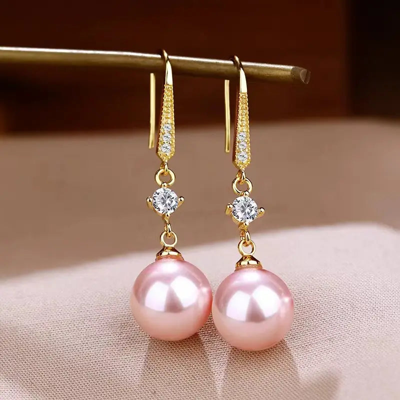 Elegant pearl and pave diamond drop earrings featuring pink pearls with gold tone hooks and diamond accents.