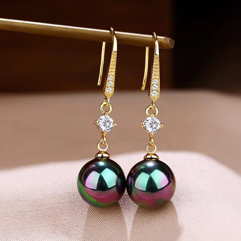 Elegant pearl and pave diamond drop earrings in gold tone featuring sparkling diamonds along the hook and large iridescent black pearls with green and purple hues.