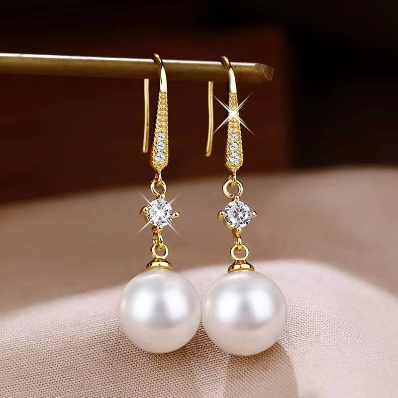 Elegant pearl and pave diamond drop earrings in gold tone featuring a central round-cut clear gemstone and dangling white pearls.