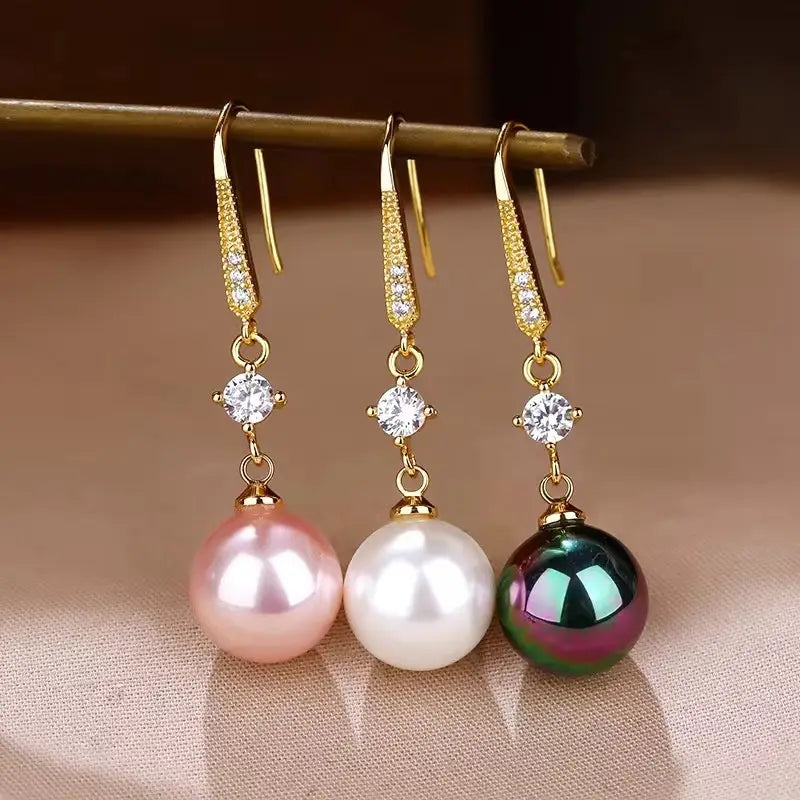 Three elegant gold-toned drop earrings each featuring a sparkling pave diamond accent and a single pearl in pink white or iridescent green.