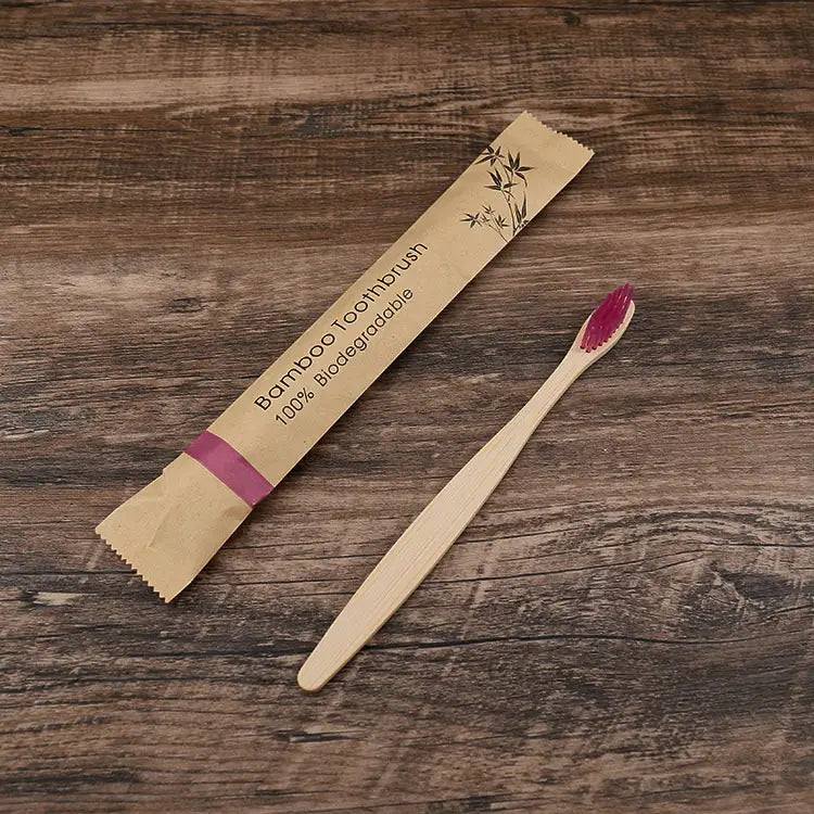 Un juego de cepillos de dientes de bambú de 10 unidades con cepillos de bambú de cerdas suaves, acabado de madera natural de tono claro y cerdas vibrantes de color rosa, envasado en una funda de papel marrón respetuosa con el medio ambiente.