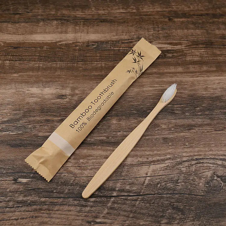 Un cepillo de dientes de bambú natural con cerdas blancas suaves fabricado con material 100 % biodegradable, en una funda de papel color canela, rotulada "cepillo de dientes de bambú" para un conjunto de 10 unidades respetuoso con el medio ambiente.