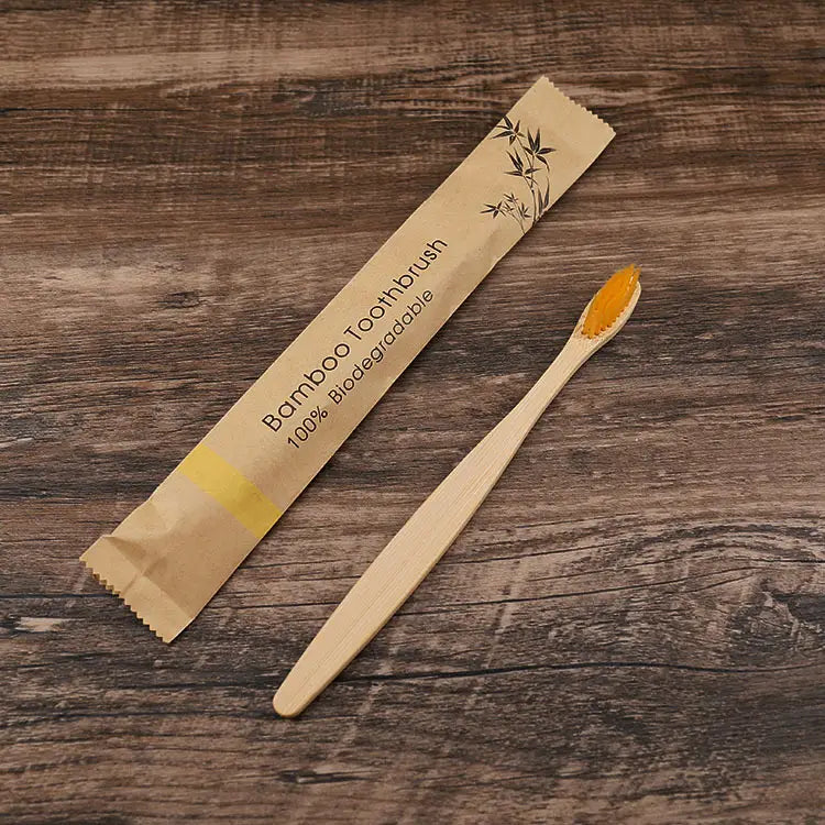 Un cepillo de dientes de bambú natural con un mango color beige claro y cerdas suaves naranjas vibrantes, envasado en una funda de papel respetuosa con el medio ambiente con diseños de hojas de bambú, correspondiente al juego de 10 unidades de cepillos de bambú con cerdas suaves respetuosas con el medio ambiente.