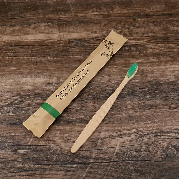 Un cepillo de dientes de bambú color beige claro con una cabeza de cerdas suaves verdes vibrantes, envasado en una funda de papel respetuosa con el medio ambiente con diseños de hojas de bambú para el juego de cepillos de dientes de bambú de 10 unidades.