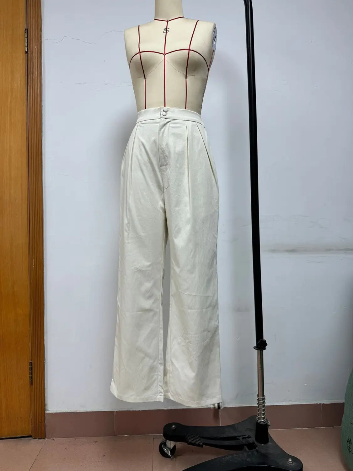 Pantalons blancs à taille haute et jambes larges, avec un devant plissé et une fermeture à boutons, présentés sur un mannequin.