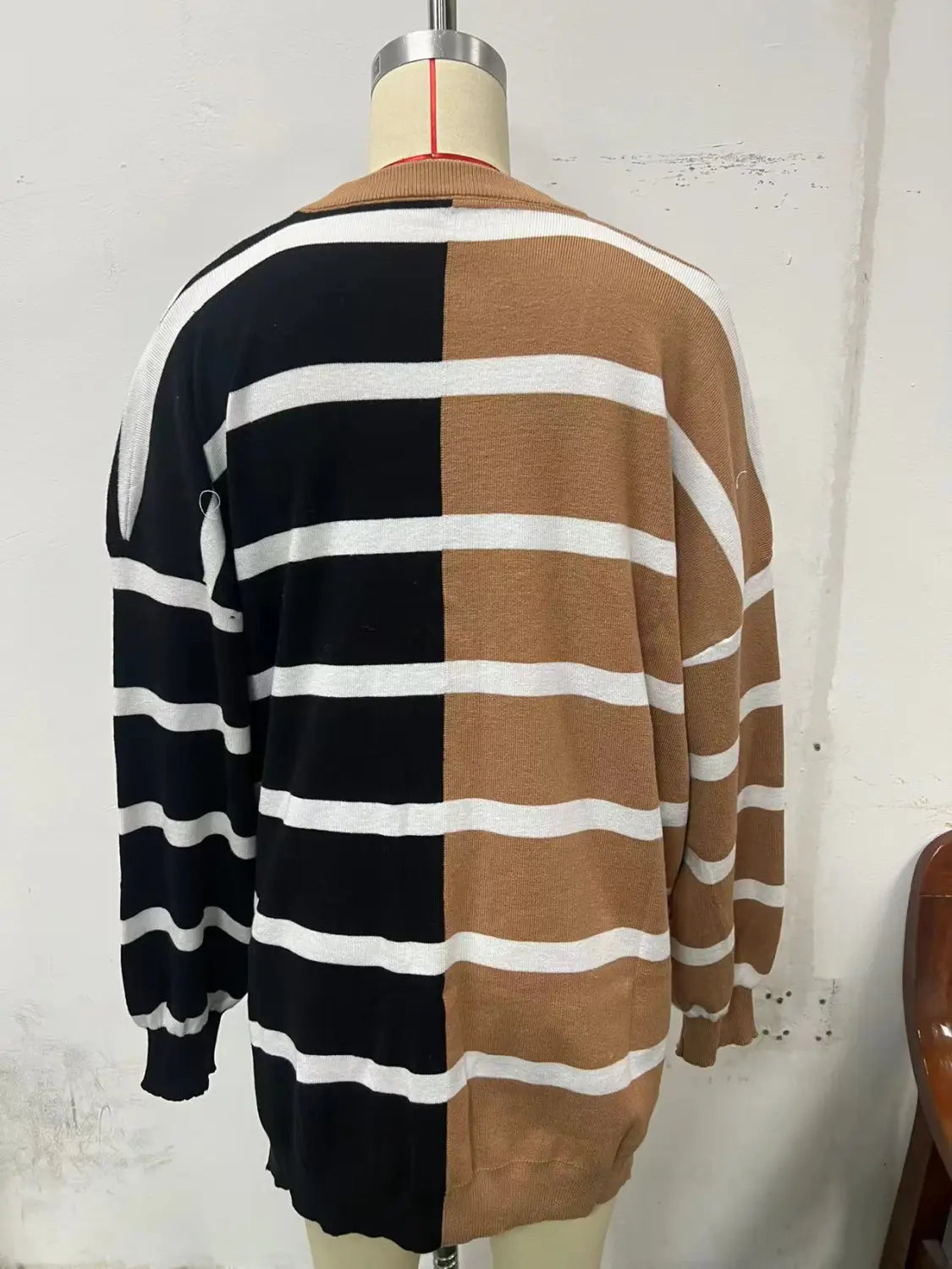 A cozy women’s oversized knit cardigan with a long sleeve black and tan color block design featuring horizontal white stripes on both sides.