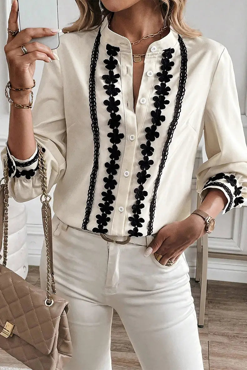 Cream-colored long sleeve blouse featuring black floral embroidery and chain detailing along the front placket and cuffs with lace trim.