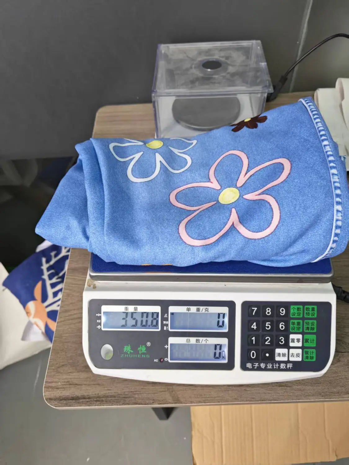 刺繍入りデニムのオーバーオール（ワイドレッグ・レトロパンツ）。刺繍入りのピンクと白の花（黄色の中心）をあしらったブルーのタオルと組み合わせています。