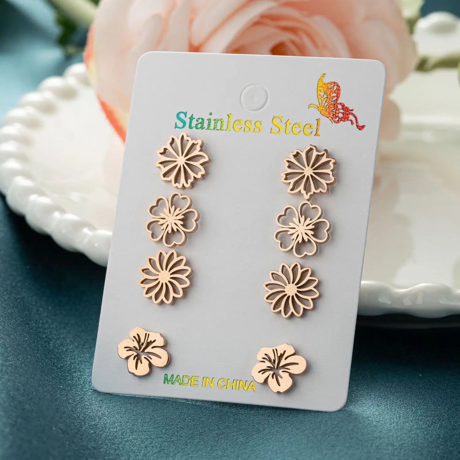 Ensemble de six boucles d’oreilles à clous en acier inoxydable à la teinte or rosé, en forme de fleur, présentées sur une carte blanche, dans un ensemble de 6 boucles d’oreilles à clous en acier inoxydable à motif floral.