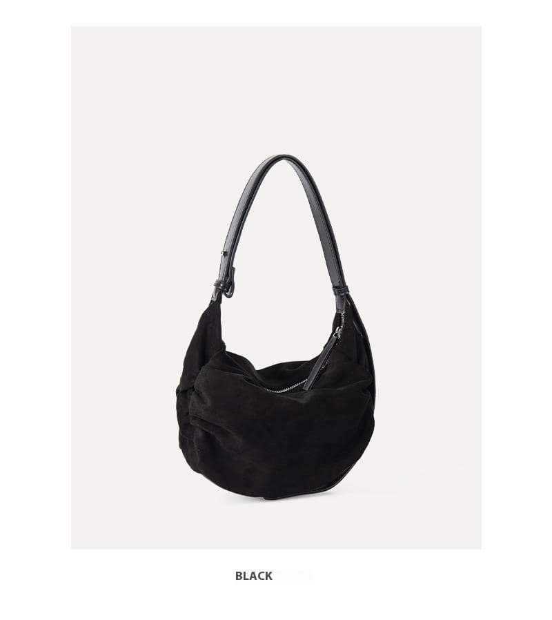 Black suede dumpling shoulder bag with sleek curved silhouette and contrasting black leather shoulder strap designed as a slouchy crossbody hobo bag.