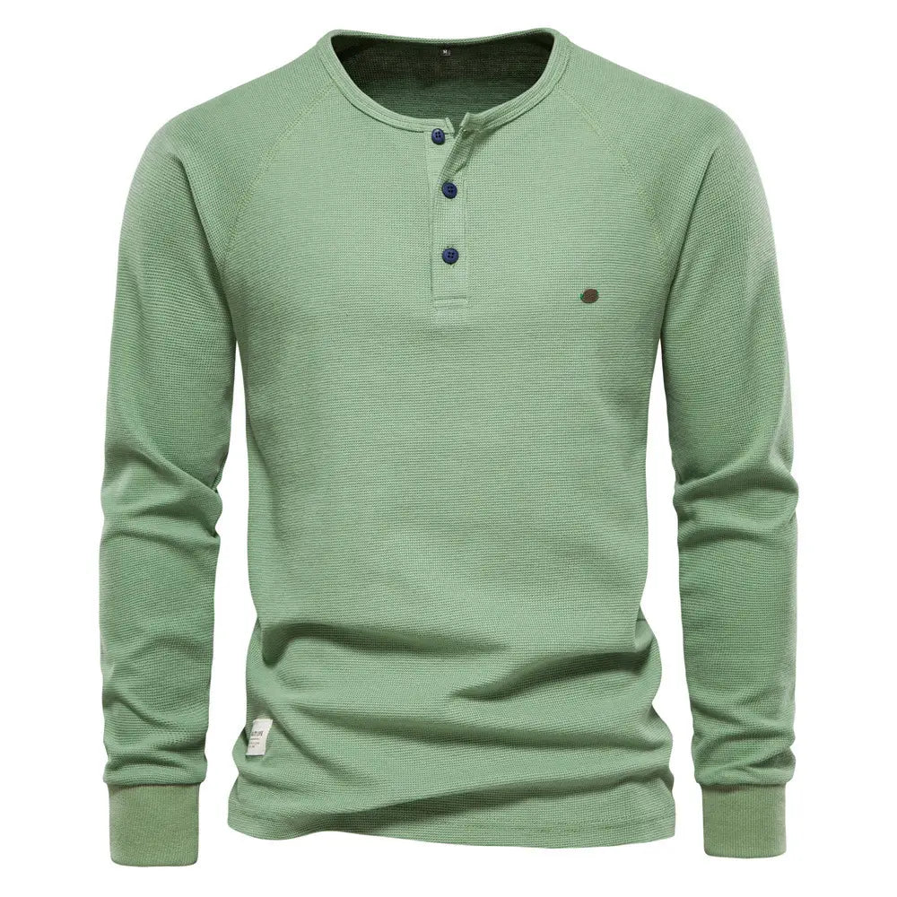 Chemise henley à manches longues côtelée pour homme, de couleur verte, avec un tissu tricoté texturé et des boutons bleu foncé.