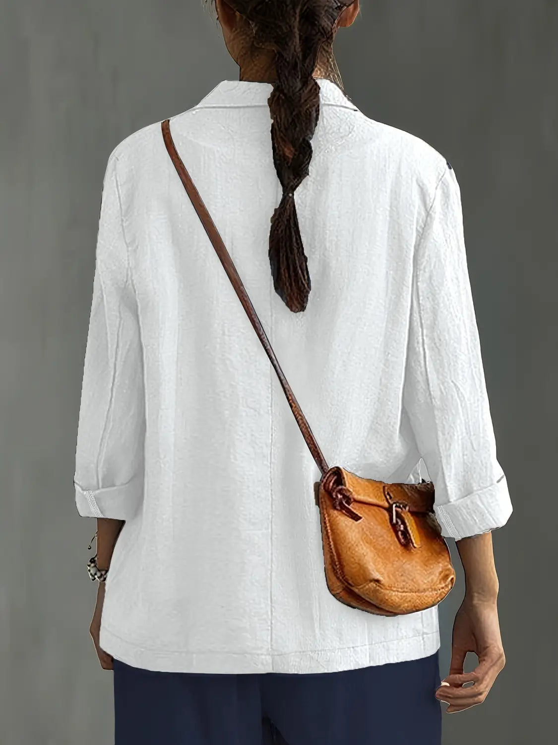 Un bolso cruzado de cuero color camel, con correa marrón y cierre ajustable con hebilla, combinado con un blazer de lino para mujer, casual y de trabajo.