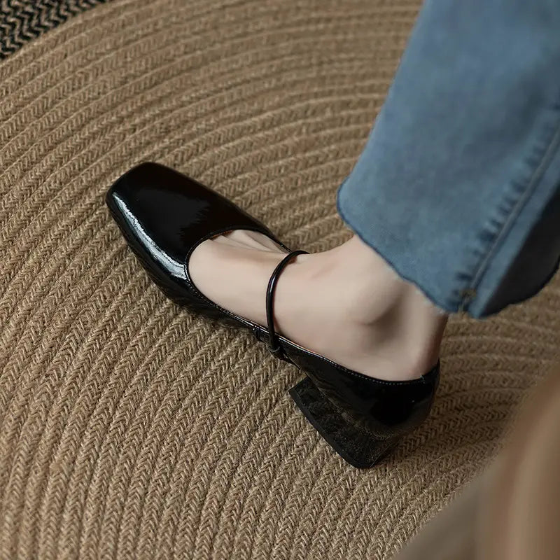 black patent leather square-toe mary jane flats with low block heels and ankle straps shown from the back side