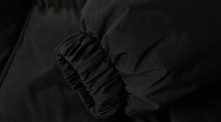 Detalle de puños de tela fruncida en negro en la chaqueta acolchada con capucha para mujer, que muestra el diseño cálido y con estilo de la chaqueta.