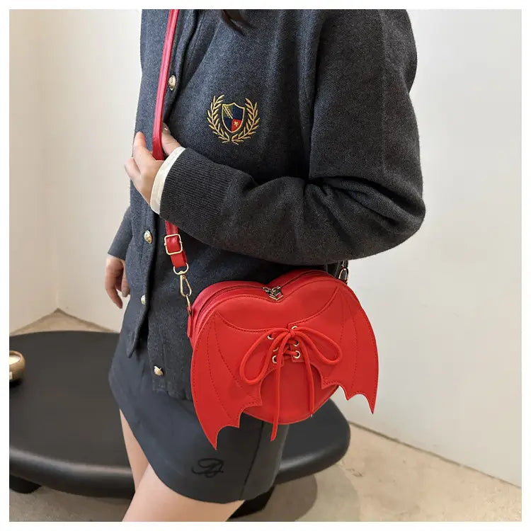 A vibrant red bat wing heart crossbody bag featuring a lace-up front and gold-tone hardware.