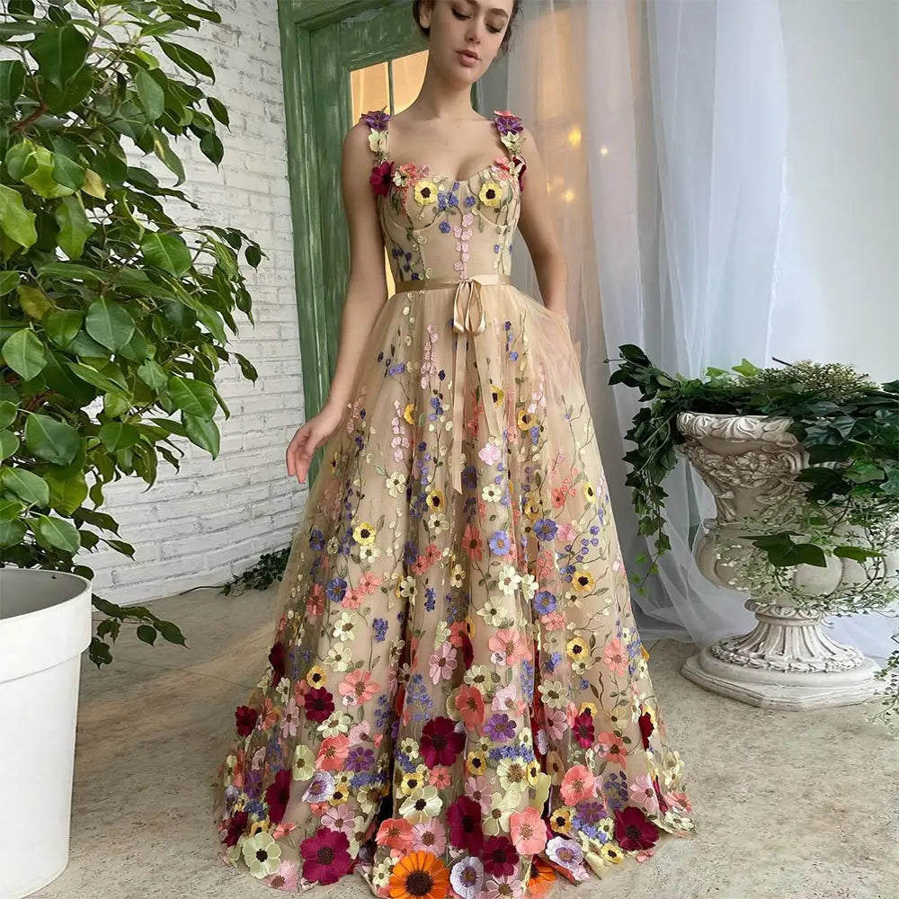 a flowing beige tulle prom gown with a sweetheart neckline adorned with vibrant three-dimensional floral appliqués in pink purple yellow and orange