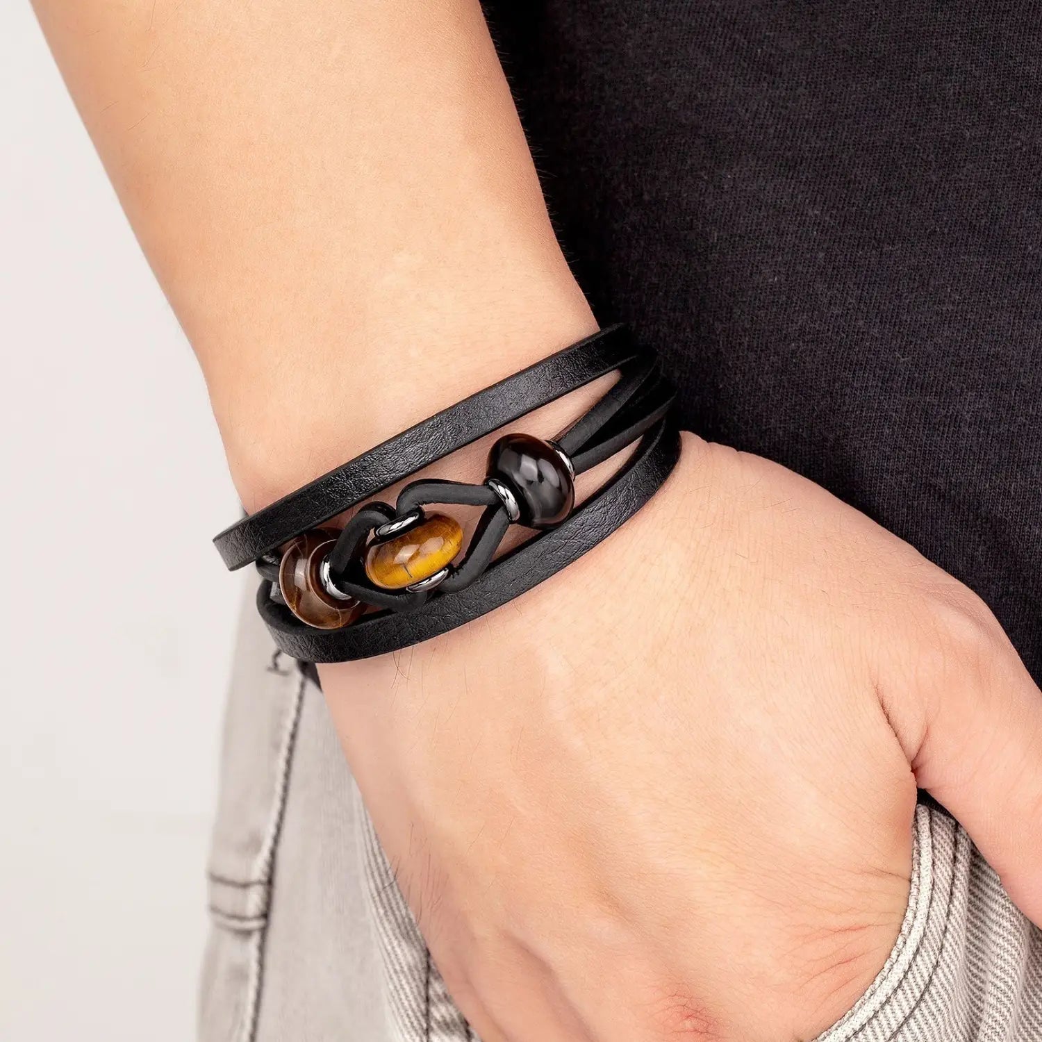 Bracelet en cuir noir à cordon, avec des perles en pierre naturelle comportant une pierre œil-de-tigre centrale et un accent de perle sombre, avec une fermeture magnétique.