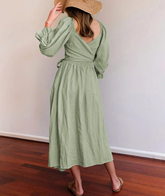 A soft sage green long-sleeved reversible midi dress with a v-neck lantern sleeve back tie and gathered waist shown from the back.