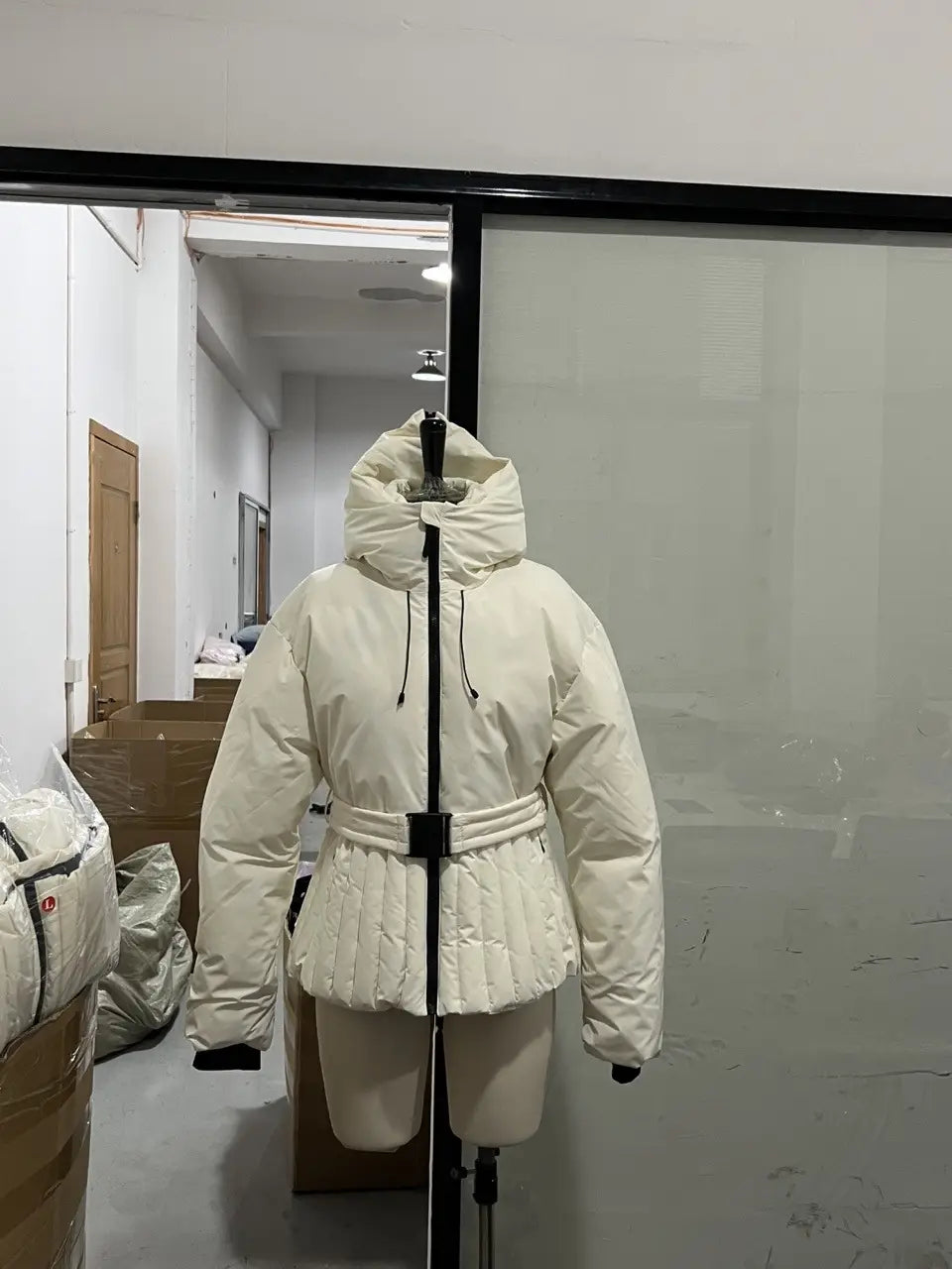Cream-colored quilted belted hooded puffer coat with black drawstrings and a cinched waist for women.
