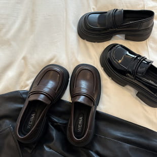 black leather loafers with a glossy finish and thick soles designed as brown leather loafers with gold buckle detail.