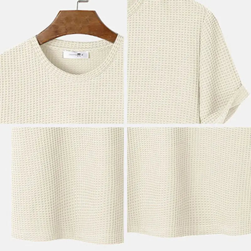 Herren-T-Shirt in Slim-Fit aus waffelgestricktem, cremefarbenem Baumwollstoff als Henley mit kurzen Ärmeln und Rundhalsausschnitt, auf einem Holzkleiderbügel hängend.