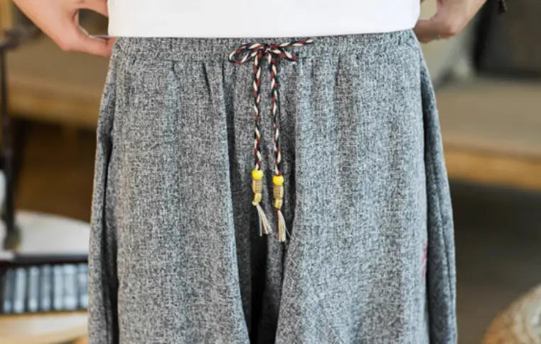 Herren graue strukturierte Leinenhosen mit geflochtenem Kordelzug und gelben Perlenakzenten, entworfen als Wide-Leg-Lantern-Harem-Shorts aus Baumwolle.