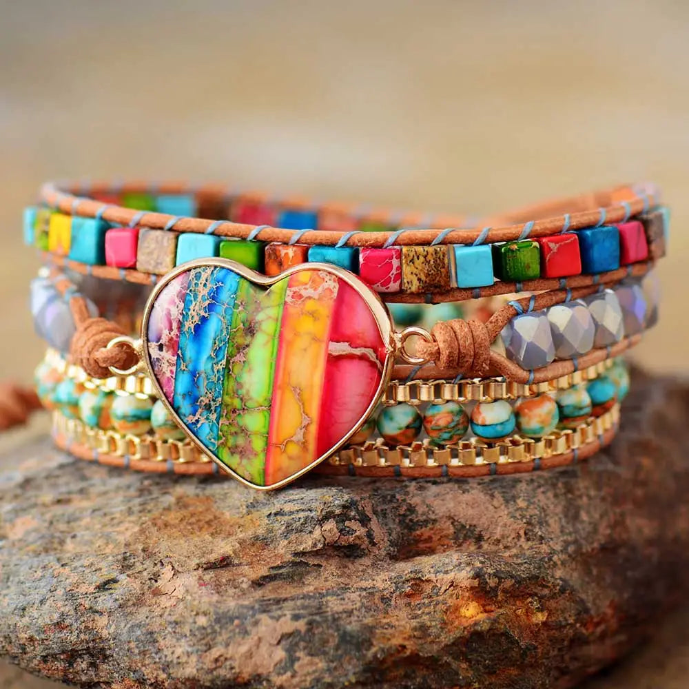 A vibrant rainbow heart imperial stone leather wrap bracelet with a multi-strand design featuring a central rainbow-colored heart pendant with gold-tone edges and layered bands of leather turquoise beads and metallic accents.