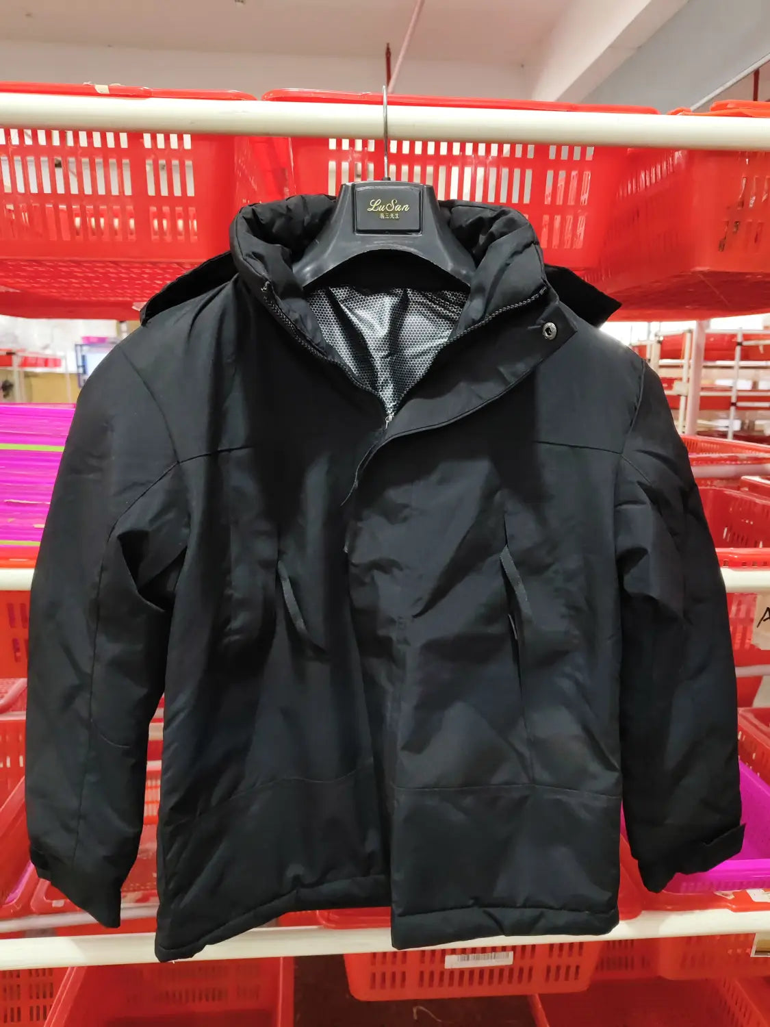 Chaqueta acolchada negra con capucha y cremallera frontal colgando sobre una percha negra para la chaqueta de caparazón impermeable 3 en 1 para parejas.