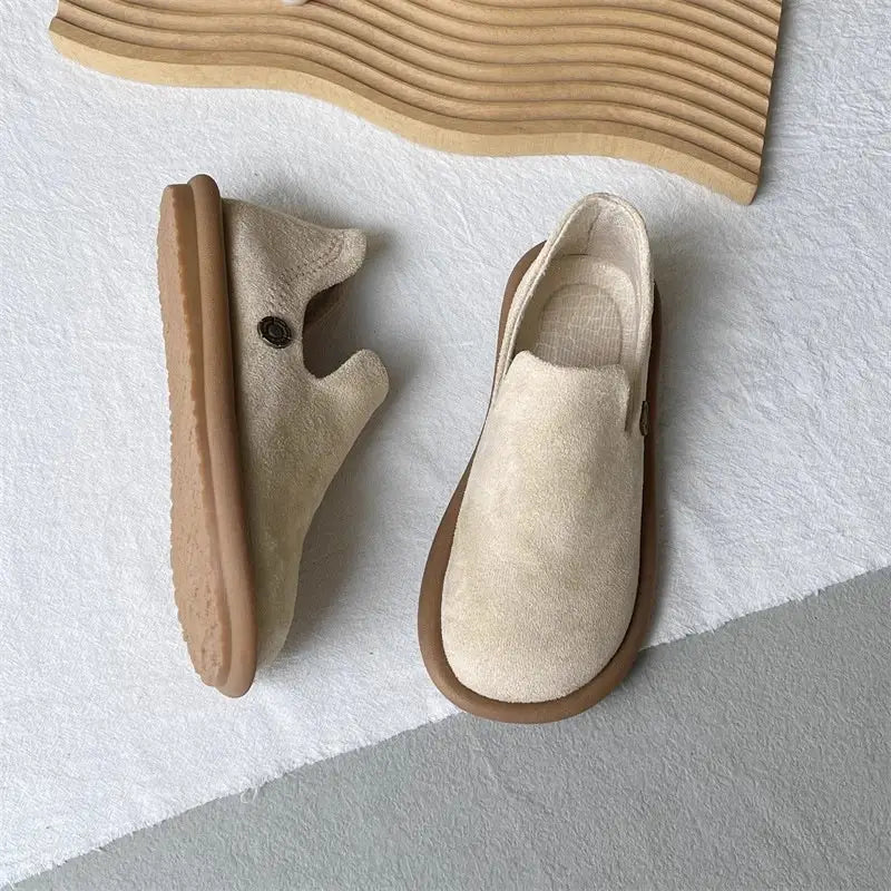 Beige Veloursleder-Slipper im Vintage-British-Stil mit niedrigem Absatz mit einer braun wirkenden Gummisohle und einem kleinen dunklen Knopf an der Seite.