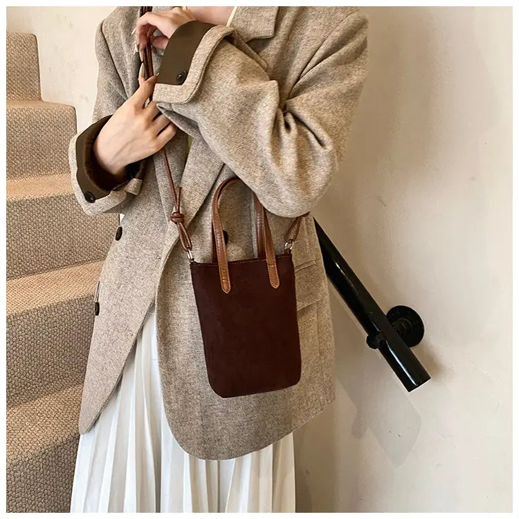 Retro leopard print suede mini bucket crossbody bag featuring brown suede with tan leather handles and an adjustable strap.