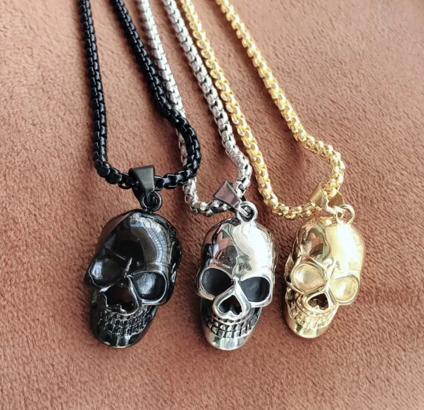 Three skull-shaped pendant necklaces in black silver and gold finishes made of titanium steel with matching chains for men and women.