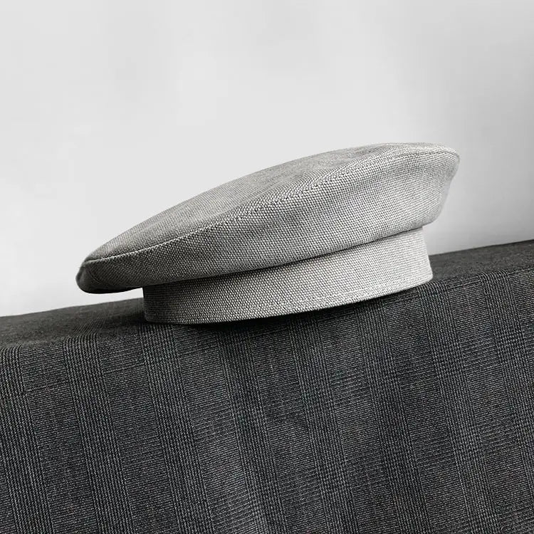 Béret en laine gris clair élégant, avec une texture tissée discrète et une calotte arrondie souple, conçu comme une casquette de peintre pour femmes.