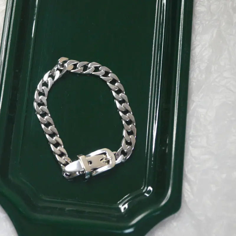 Silver-toned curb link women’s platinum plated stainless steel bracelet featuring a polished metal buckle clasp.