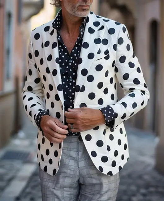 Ein Mann, der eine Hahnentritt-Slim-Fit-Anzugjacke in Weiß mit kräftigen schwarzen Punkten trägt, kombiniert mit einem passenden gemusterten Hemd und grauen Karohosen.