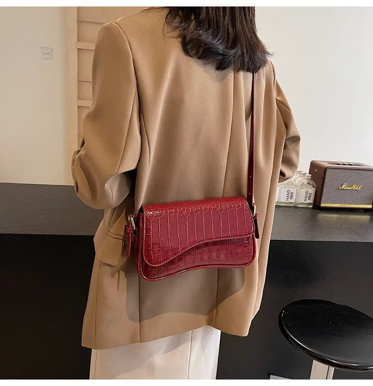 A vibrant red leather messenger bag with crocodile texture and a sleek modern design ideal for minimalist crossbody use.