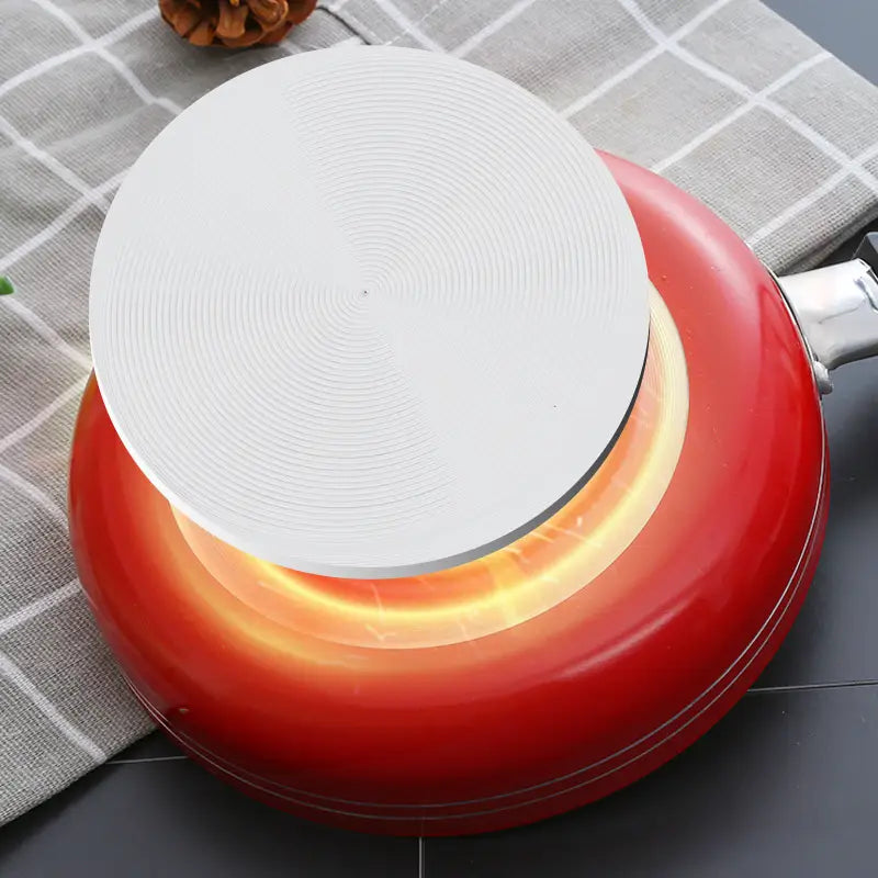 white circular heat diffuser on top of a red mini non-stick frying pan made of aluminum cookware set