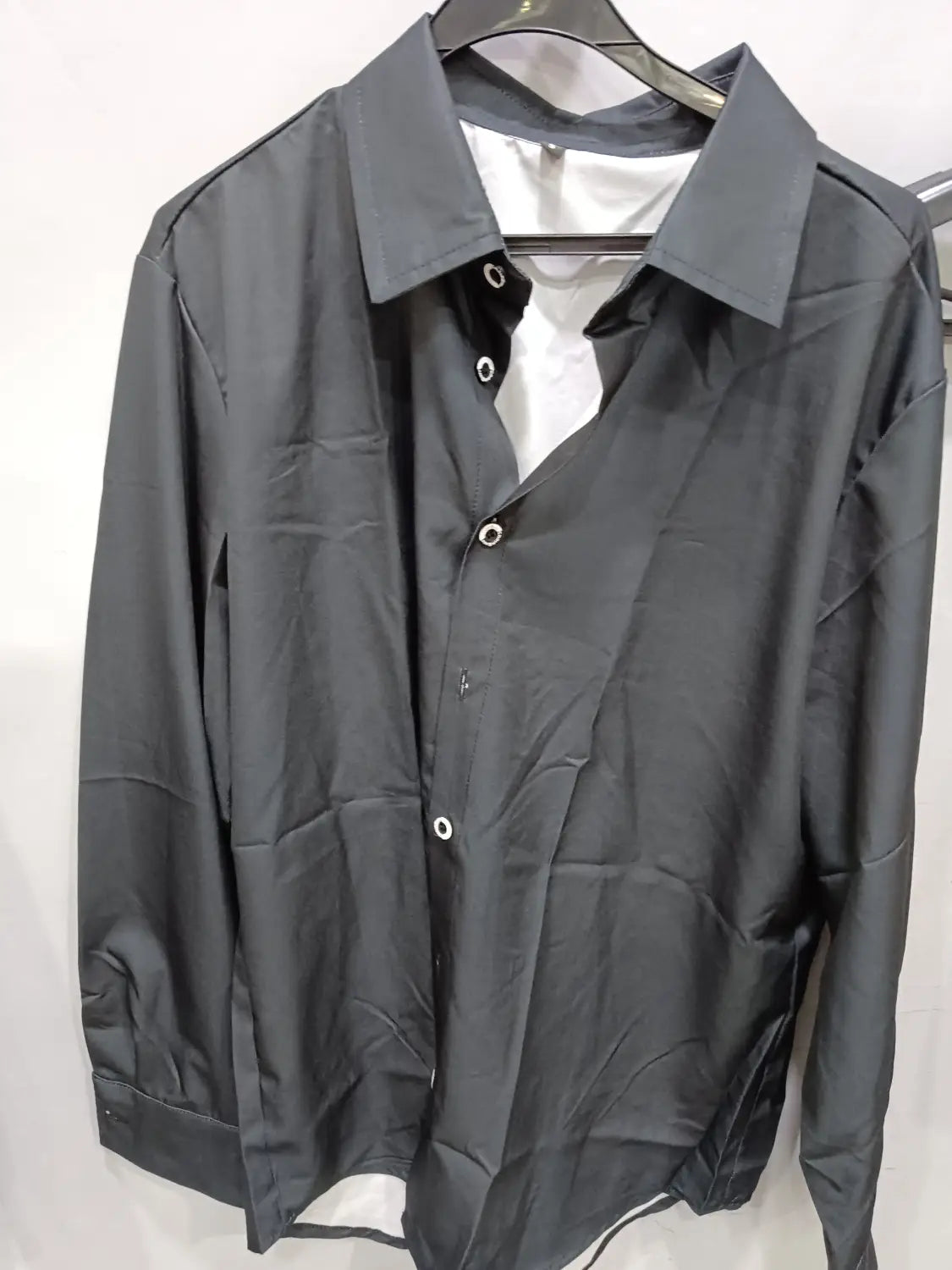 Elegantes schwarzes Herren-Business-Kleidhemd ohne Bügeln mit langen Ärmeln, einem formstabilen Kragen und weißen Knöpfen, die ordentlich an einem Bügel hängen.