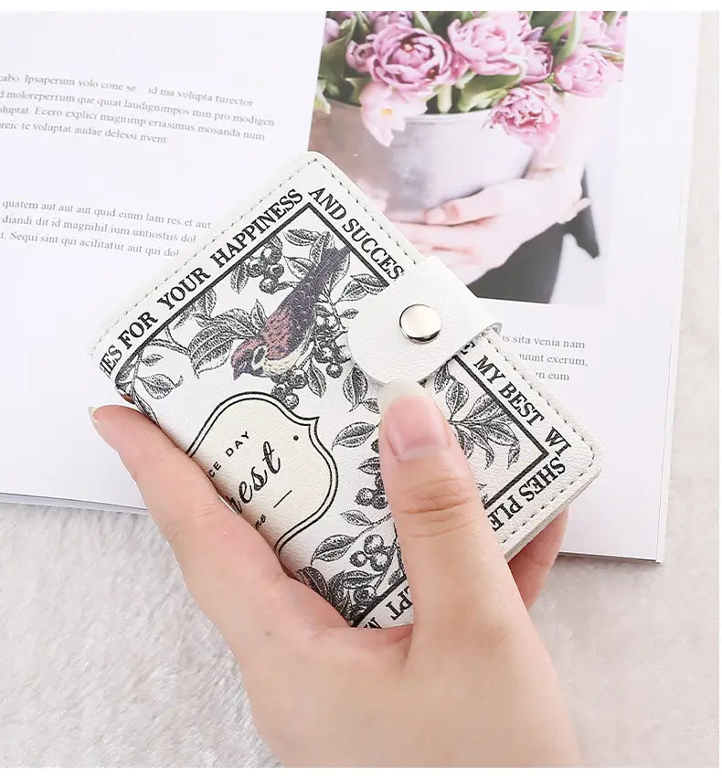 White leather vintage floral pu leather multi slot card holder wallet with black bird and botanical print design and silver-toned snap closure.
