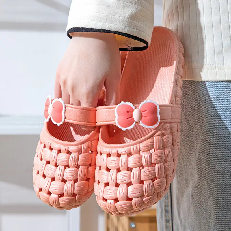 Pink woven plastic slide sandals with decorative bow ties on the strap designed as summer PVC beach slide sandals.