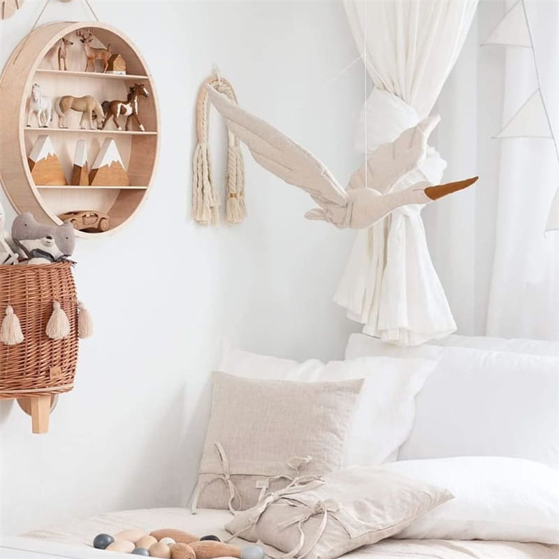 Jouet en peluche de cigogne souple blanc cassé, avec un bec brun et de délicates franges suspendues au mur, conçu comme un oreiller d’animal en forme de cygne blanc.