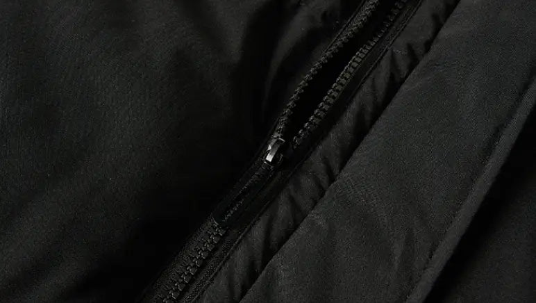 Cremallera negra con una pieza de tirador metálica integrada en la costura de una tela oscura de una chaqueta acolchada con capucha para mujer.
