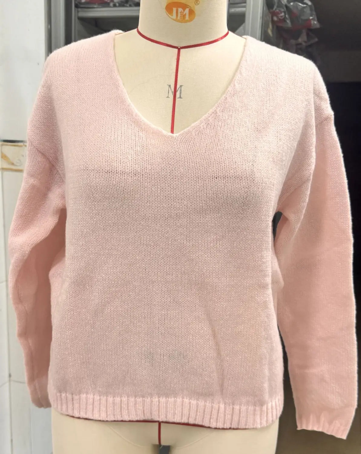 Weicher rosafarbener Strickpullover mit V-Ausschnitt und überschnittener Schulterpartie mit langen Ärmeln und gerippten Bündchen, auf einer Schneiderpuppe präsentiert.