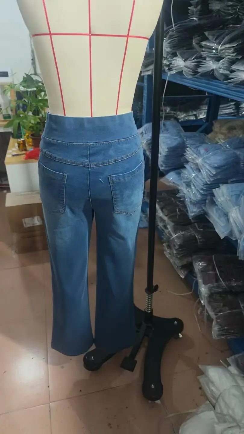 Blaues Denimjeans mit hoher Taille und ausgestellten Beinen, auf einer Schaufensterpuppe präsentiert; mit geradlinigen Schnitten gestaltet und aus strapazierfähigem Denim-Gewebe gefertigt.