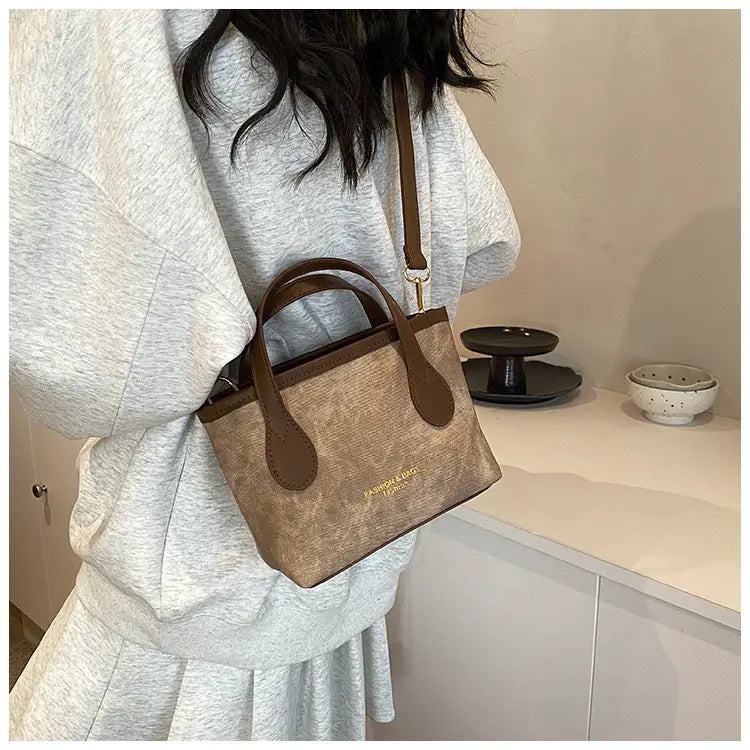 Beige textured canvas retro bucket bag mini tote with brown leather handles and trim featuring a subtle gold logo on the front.