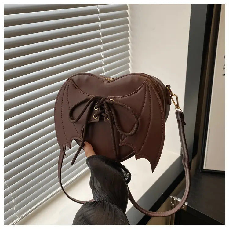 Brown bat wing heart crossbody bag made of leather with a lace-up front detail and adjustable leather straps.