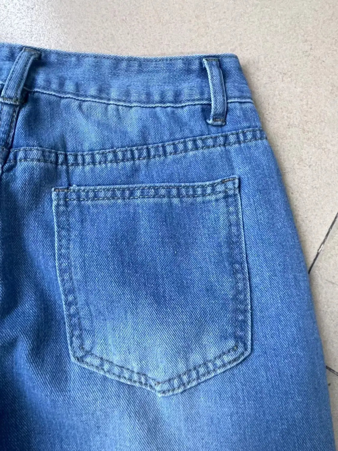Back side of distressed high rise wide leg denim jeans in medium-wash blue with classic back pocket and visible stitching.