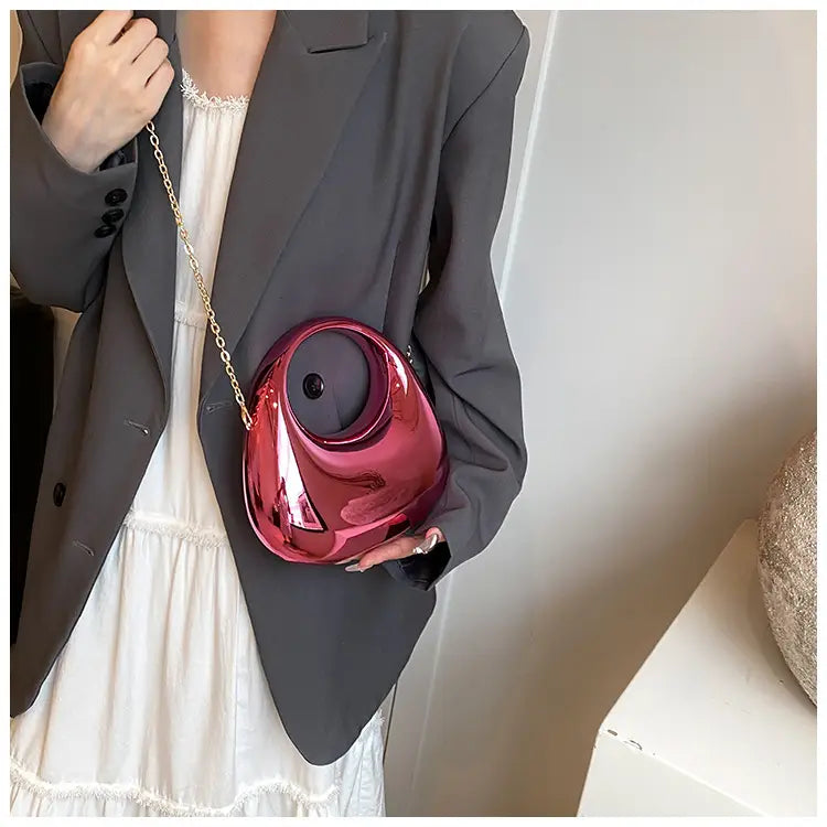A glossy vibrant red egg-shaped acrylic handbag with a metallic gold chain strap and clutch design.